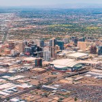 Aerial view of downtown Phoenix, Arizona, with high-rise buildings and a street grid stretching toward hazy mountains.