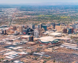 Aerial view of downtown Phoenix, Arizona, with high-rise buildings and a street grid stretching toward hazy mountains.