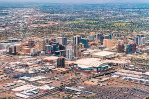 Aerial view of downtown Phoenix, Arizona, with high-rise buildings and a street grid stretching toward hazy mountains.