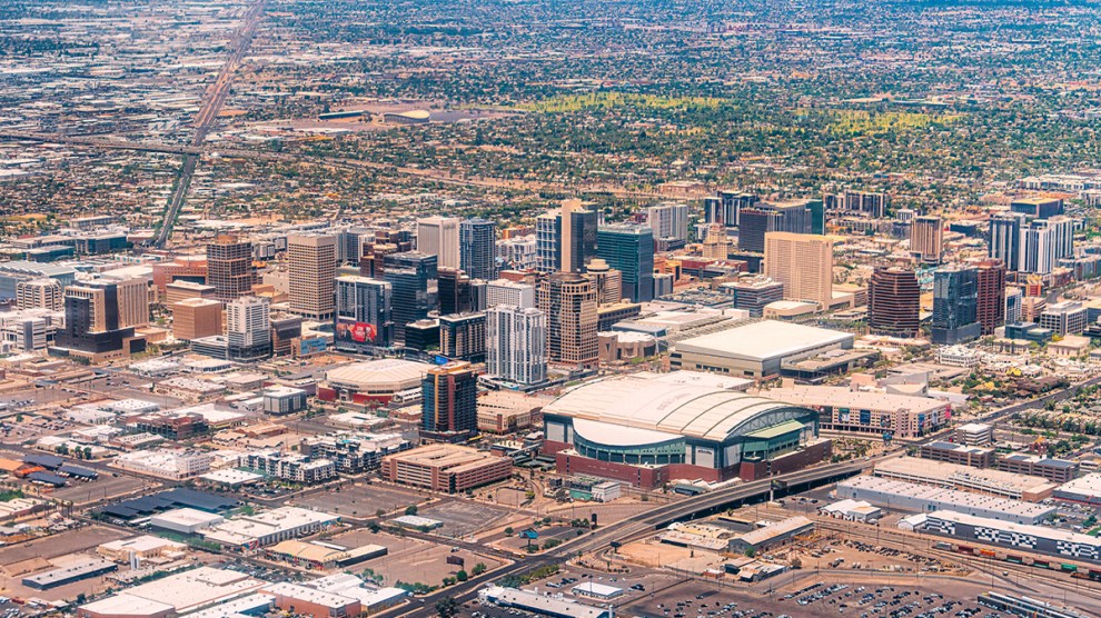 Aerial view of downtown Phoenix, Arizona, with high-rise buildings and a street grid stretching toward hazy mountains.