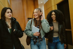 Group of young women arriving at a library or a university in New York, carrying laptops and study materials. Real students preparing to study together as part of everyday student lifestyle.