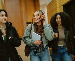 Group of young women arriving at a library or a university in New York, carrying laptops and study materials. Real students preparing to study together as part of everyday student lifestyle.