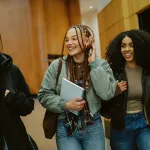 Group of young women arriving at a library or a university in New York, carrying laptops and study materials. Real students preparing to study together as part of everyday student lifestyle.