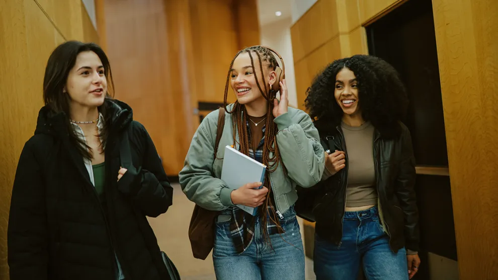 Group of young women arriving at a library or a university in New York, carrying laptops and study materials. Real students preparing to study together as part of everyday student lifestyle.